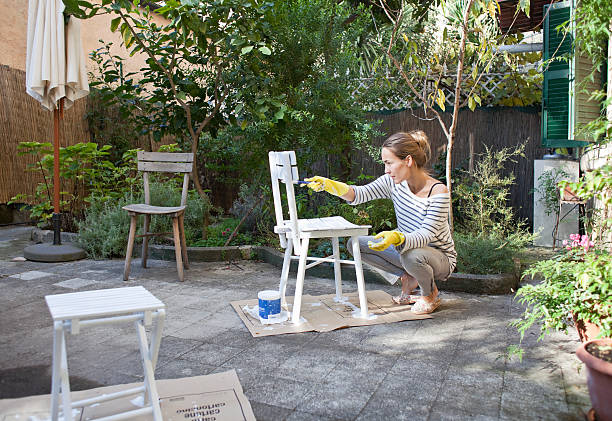 Jeune femme qui repeint son mobilier de jardin en bois